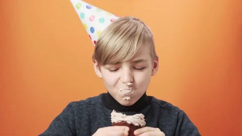 Young boy in birthday hat blows out the candle on the cupcake and eats it. Stock Footage 164380298