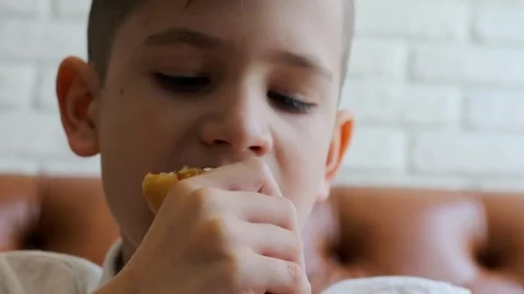 Young boy bites and chews bun during eat in cafe. Stock Footage 299631710