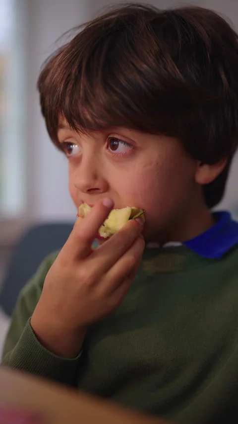 Young boy bites into a fresh apple while looking aside at home, enjoying a .. Stock Footage 343650212
