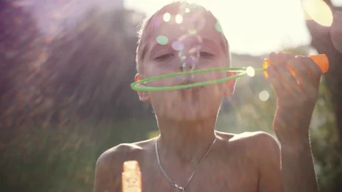 Young boy blowing bubbles outdoors on sunny day in summer on sunshine background Видео 72651523