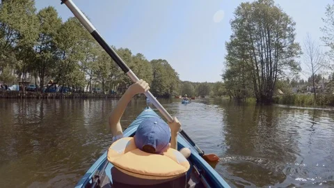 Young boy in blue cap rowing kayak on calm river out for an adventure Stock Footage 123686337