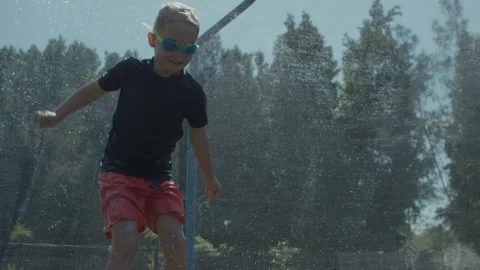 Young boy bouncing on trampoline playing in summer with water fun and games Stock Footage 135796663