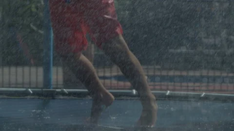 Young boy bouncing on trampoline playing fun with water hose. Video stock 135808001