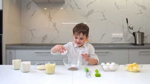 Young boy breaking eggs into a mixing bowl with a look of concentration as he Stock Footage 128833440