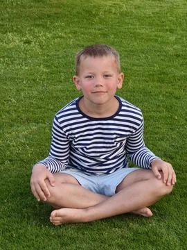Young boy with a bright, open expression sits on lush green grass, his rela.. Stock Photos