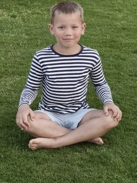 Young boy with a bright, open expression sits on lush green grass, his rela.. Stock Photos