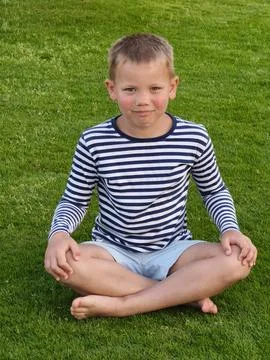 Young boy with a bright, open expression sits on lush green grass, his rela.. Stock Photos