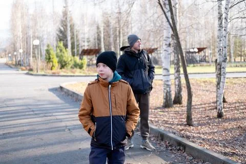 Young boy in a brown winter jacket and his father standing on an asphalt fo.. Stock Photos