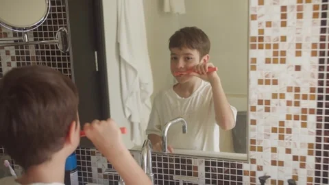 Young boy brushing his teeth with a toothbrush in a bright bathroom at home Stock Footage 348228198