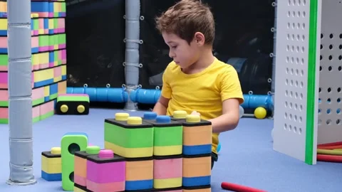 A young boy builds a colorful structure with soft blocks in a playroom. The Video stock 308627759