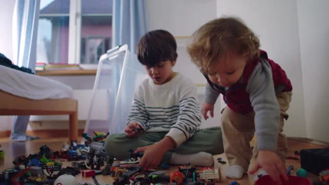 Young boy builds a construction set on the bedroom floor as his toddler sib.. Video stock 343655386