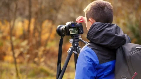 A young boy, camera and tripod in hand, captures a tranquil autumn-winter w.. 库存影片 254805098