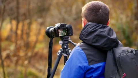 Young boy, camera and tripod, capturing serene autumn-winter woodland with .. 库存影片 254805316