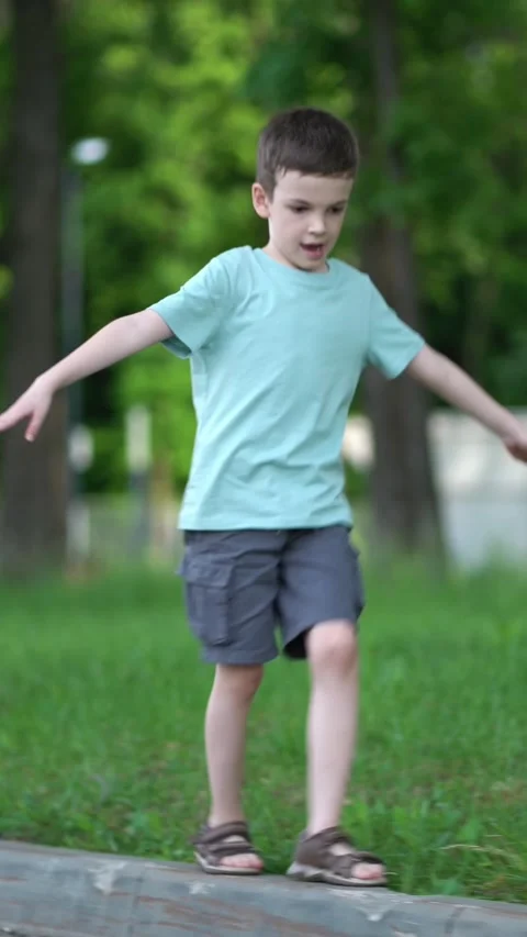 Young boy carefully balances on a park curb with arms outstretched Stock Footage 341708657