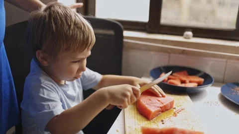 Young boy carefully cutting watermelon with a knife Stock Footage 319419559