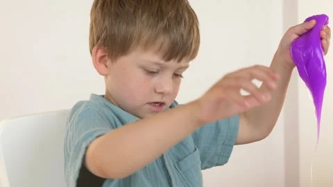 Young boy carefully examines stretched purple slime while observing its texture Stock Footage 345652008