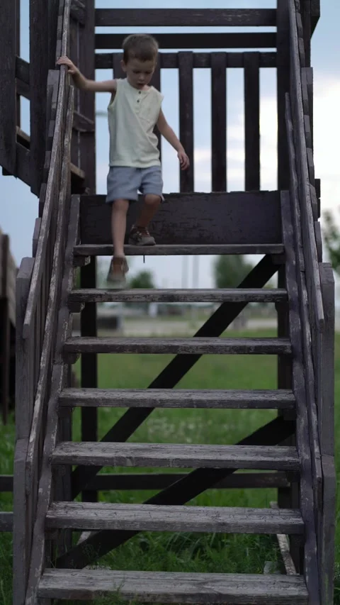 Young boy carefully steps down weathered wooden stairs outdoors Stock-Footage 341409969