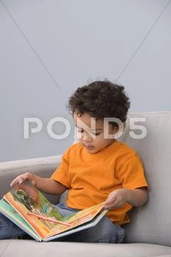 Young boy in chair reading book Stock Photos