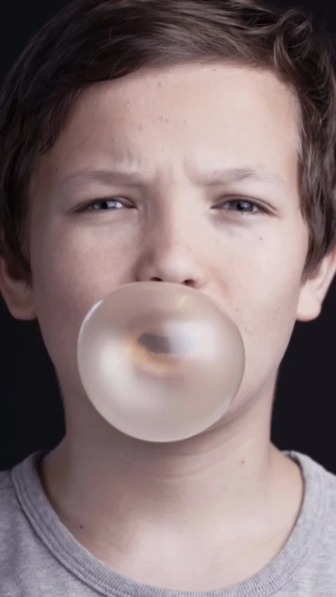 Young boy chewing bubble gum and blowing a large translucent bubble. Stock Footage 344768277