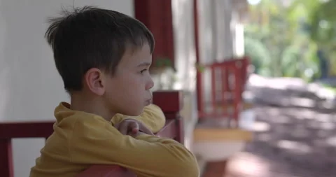 Young boy chewing gum looking off low city appartment balcony - side profile Stock Footage 320923314