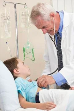 Young boy child patient in hospital bed & male doctor Stock Photos