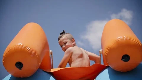 A young boy child waving his hand from the top of a water slide at playground Stock Footage 267615046