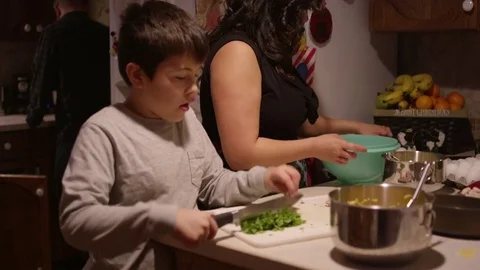 A young boy chopping vegetables in the kitchen with his mother Stock Footage 70716693