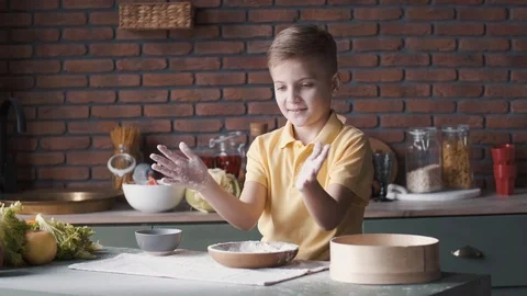 Young boy is clapping hands in flour cooking in a kitchen Stock Footage 128850660