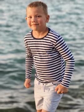 Young boy in a classic striped shirt stands confidently sea, his varied exp.. Stock Photos