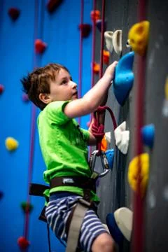 Young boy climbing up on practice wall in indoor rock gym Stock Photos