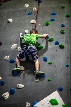 Young boy climbing up on practice wall in indoor rock gym Stock Photos