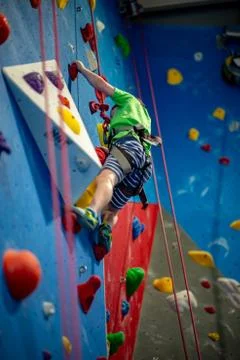 Young boy climbing up on practice wall in indoor rock gym Stock Photos