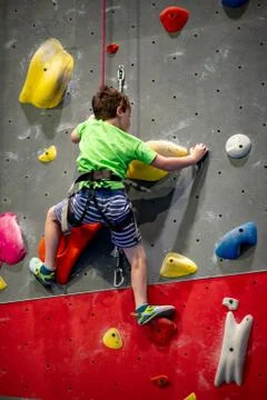Young boy climbing up on practice wall in indoor rock gym Stock Photos