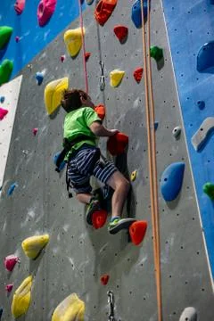 Young boy climbing up on practice wall in indoor rock gym Stock Photos