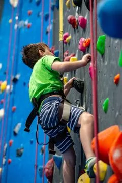 Young boy climbing up on practice wall in indoor rock gym Stock Photos