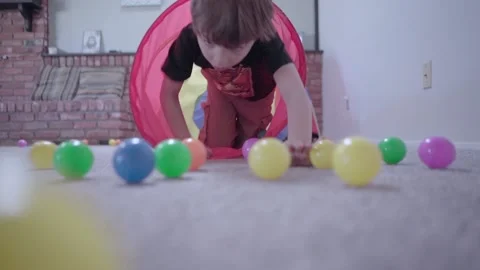 Young boy climbs through a tunnel pushing colored platic balls out. Video stock 169734448