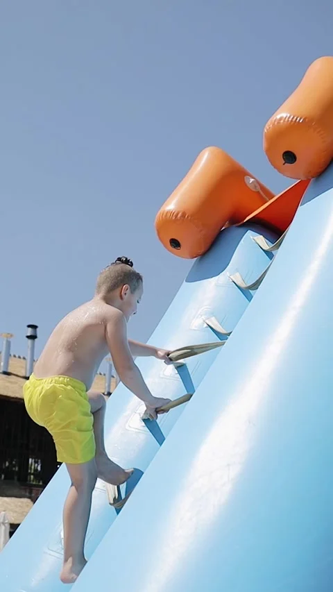 A young boy climbs up of a water slide at a playground in an aqua park Stock Footage 267762085