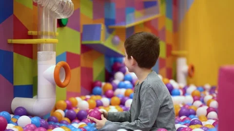 Young boy in colorful ball pit reaches for ball from tube at indoor playground.  Video stock 337006349