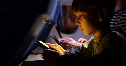 Young boy concentrated on reading his electronic book during night flight Stock Footage 303992026