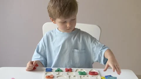 Young boy concentrates on learning the alphabet, thoughtfully placing colorful Stock Footage 318294313