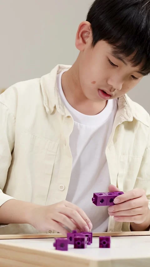 Young Boy Concentrating While Playing with Purple Interlocking Building Blocks Vídeo Stock 329261944