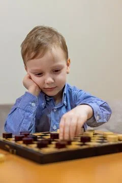 Young boy concentrating while playing checkers. A young boy in a blue checkered Stock Photos