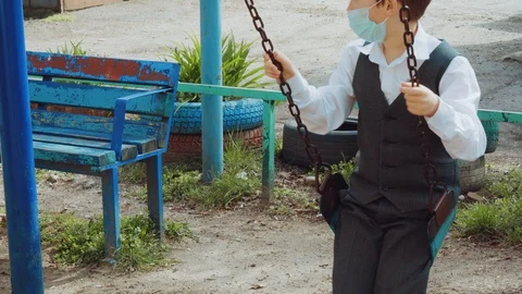 Young boy corrects protective face mask, rides on swing with pleasure at sun day Stock Footage 127832221