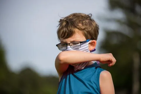Young boy coughs into arm while wearing a mask during pandemic Foto stock