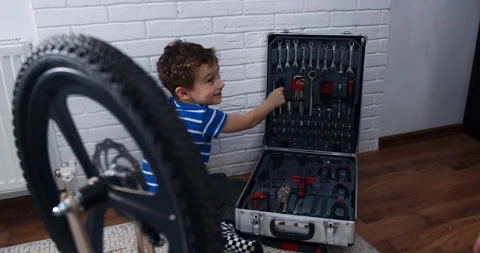 A young boy creatively explores tools in a suitcase to fix a tire Stock Footage 306847049