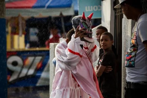 Young boy in devil costume hides from rain on city street at dominican carniv 写真素材