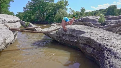 Young boy doing front flip into river from rocky bank Stock Footage 142394624