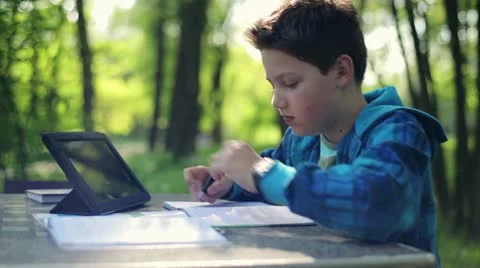 Young boy doing homework and using tablet computer in the park HD Stock Footage 10987104