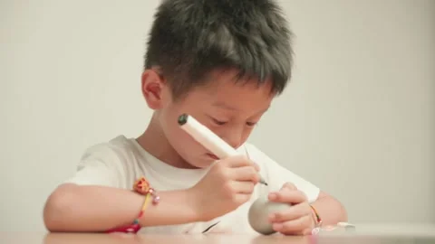 Young Boy Drawing Design on Grey Ceramic Egg with Marker Stock Footage 339069269