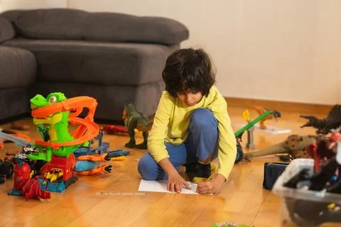 Young boy drawing on paper surrounded by toys at home Foto stock